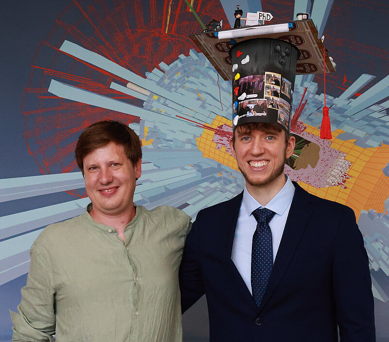Two men smiling, one of them is wearing a graduation cap.
